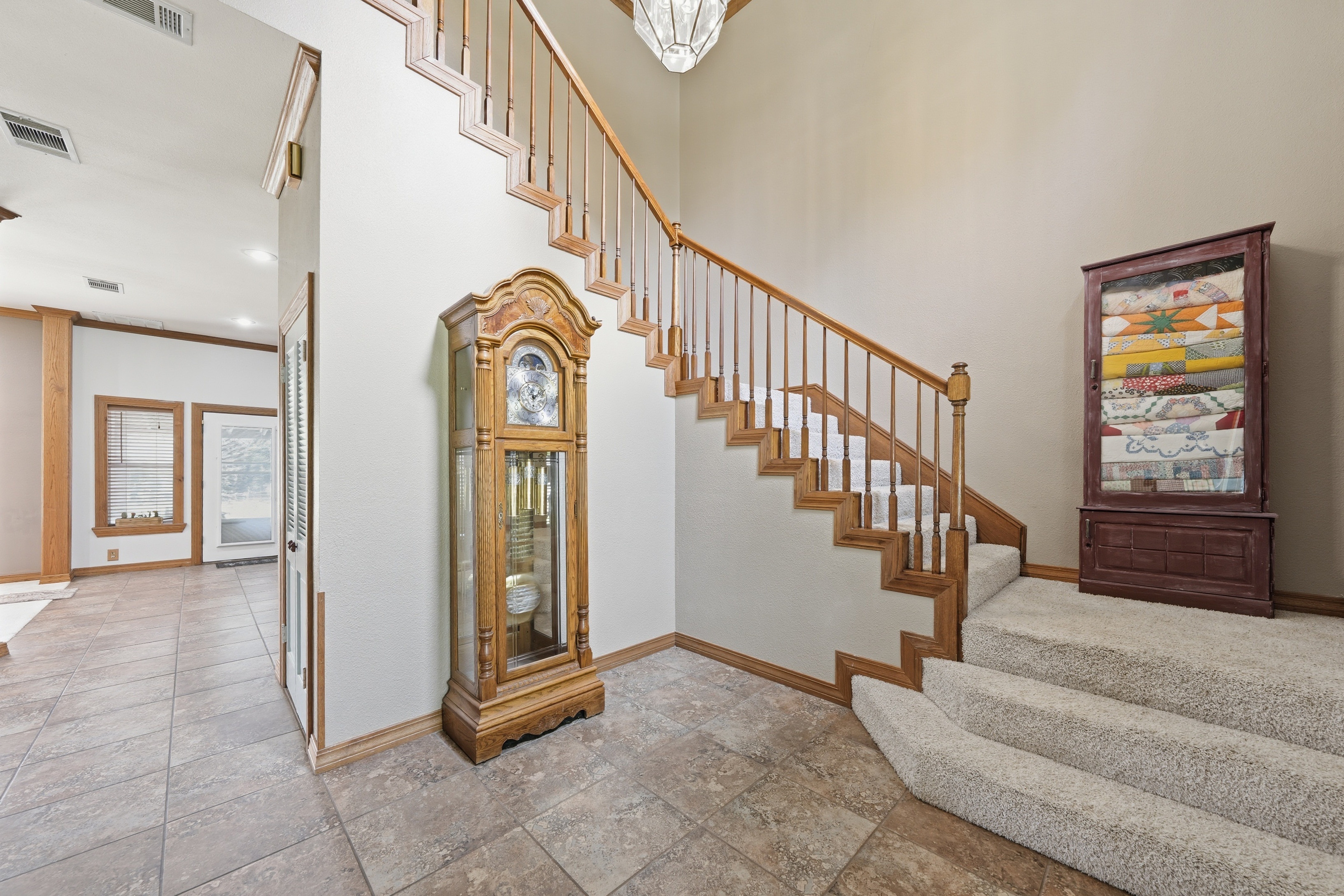 View into the living and family wing showing 18-inch tile flooring, brick fireplace, and stained crown molding.