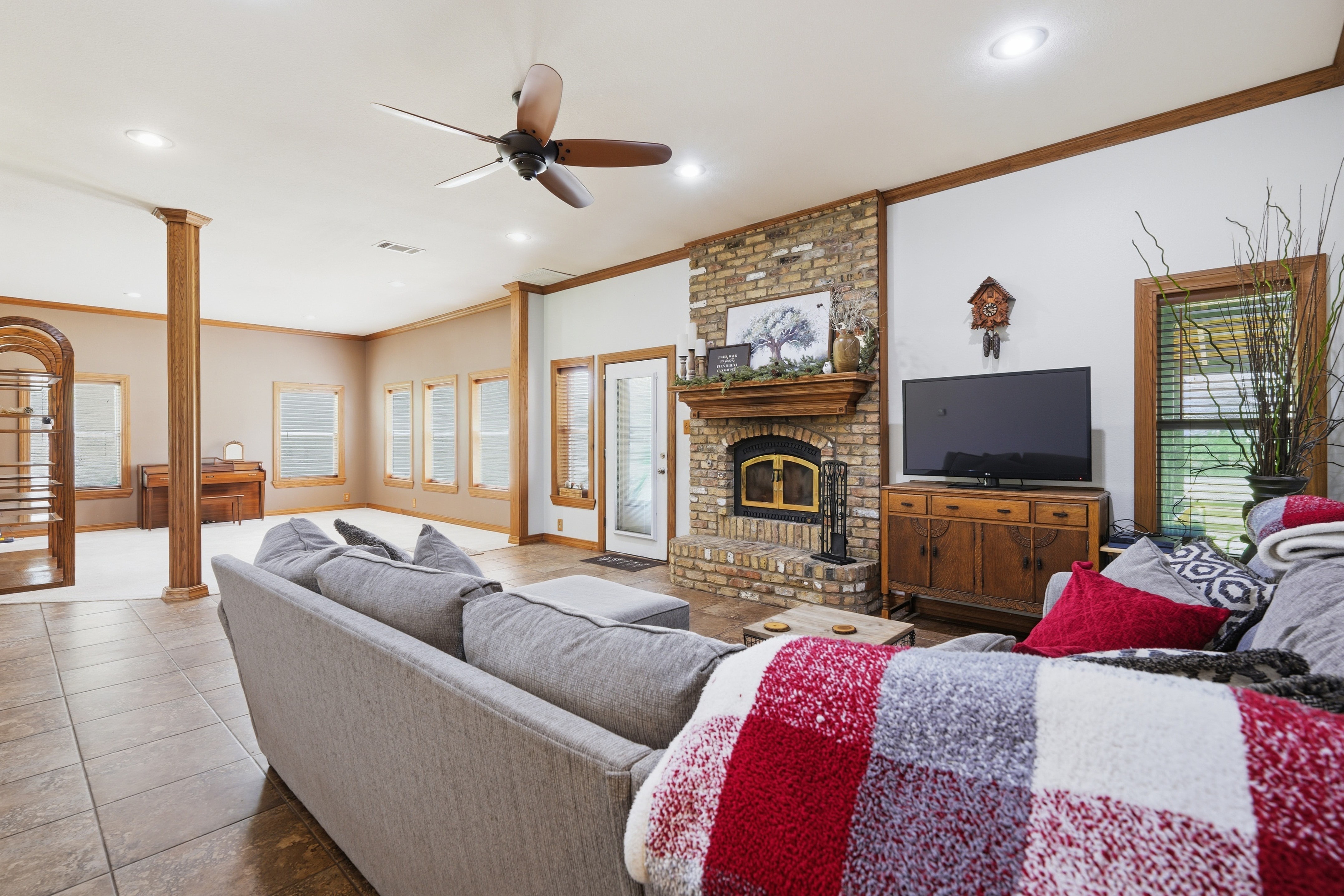 Fireside seating in the living room with brick mantel, mounted television, and tile flooring extending to the rear door.