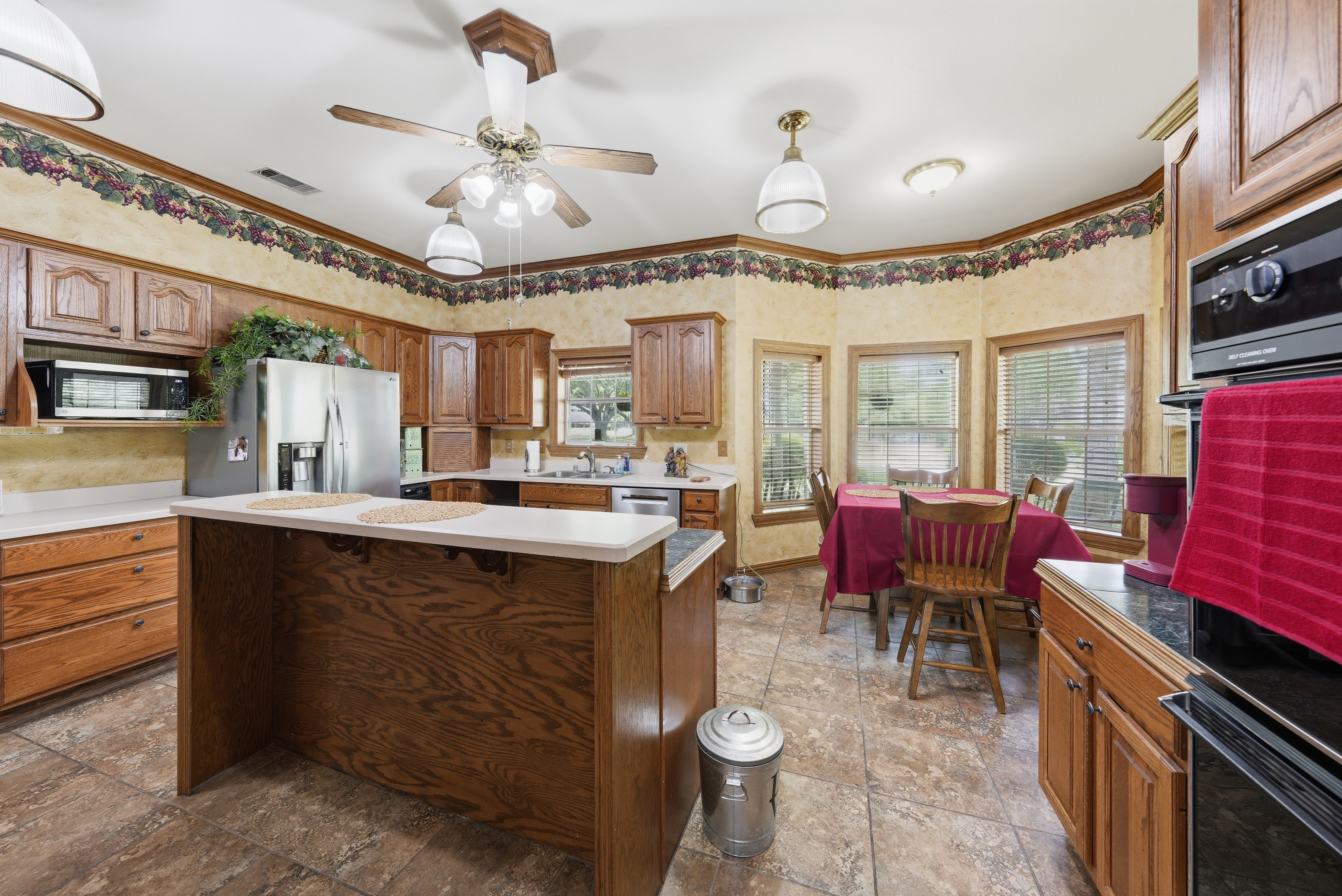 Kitchen cooktop and double oven with stained raised-panel cabinetry and grape-vine border trim.