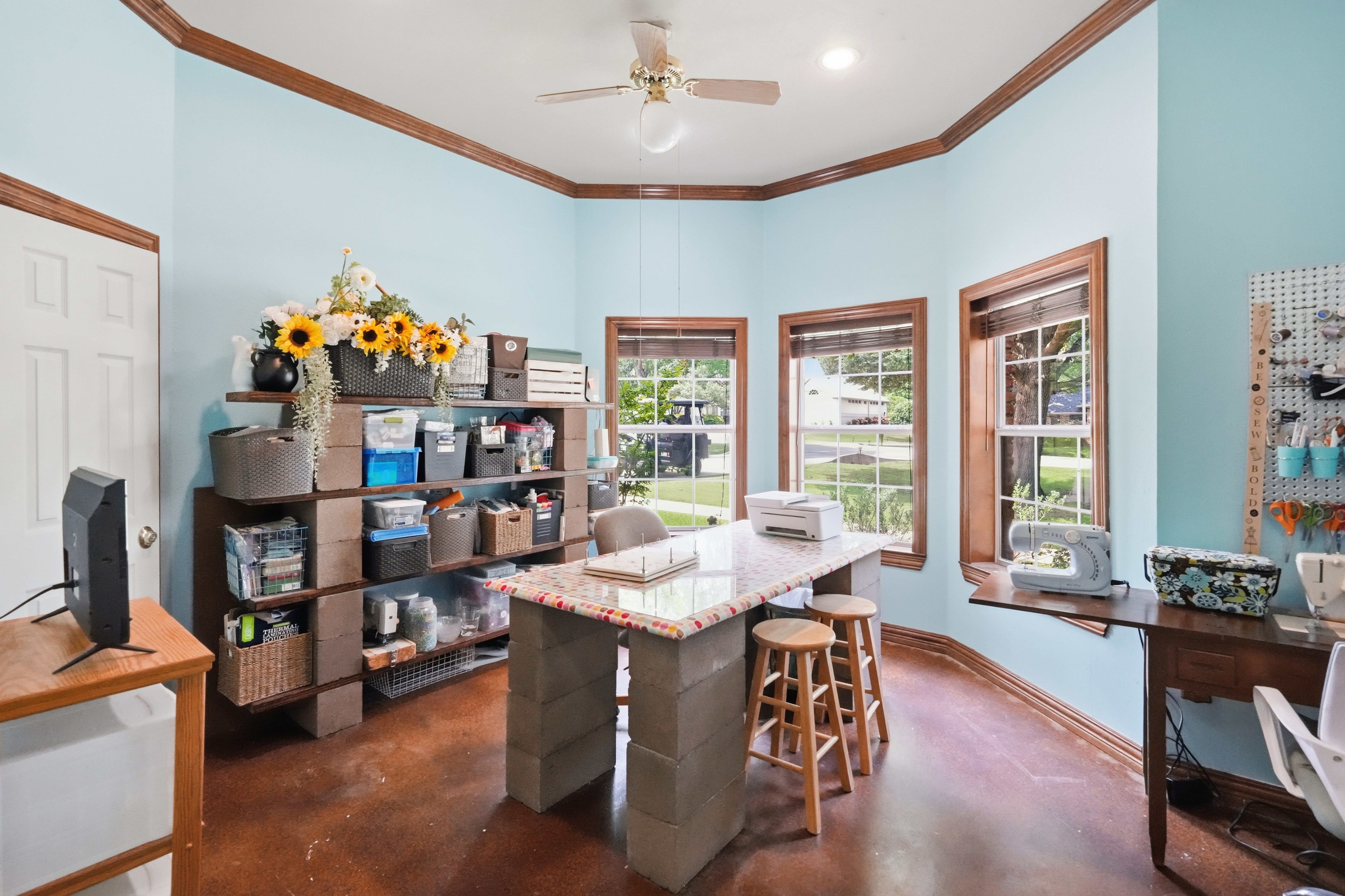 Home office with three large bay windows overlooking the front yard, stained concrete floors, and stained wood trim.