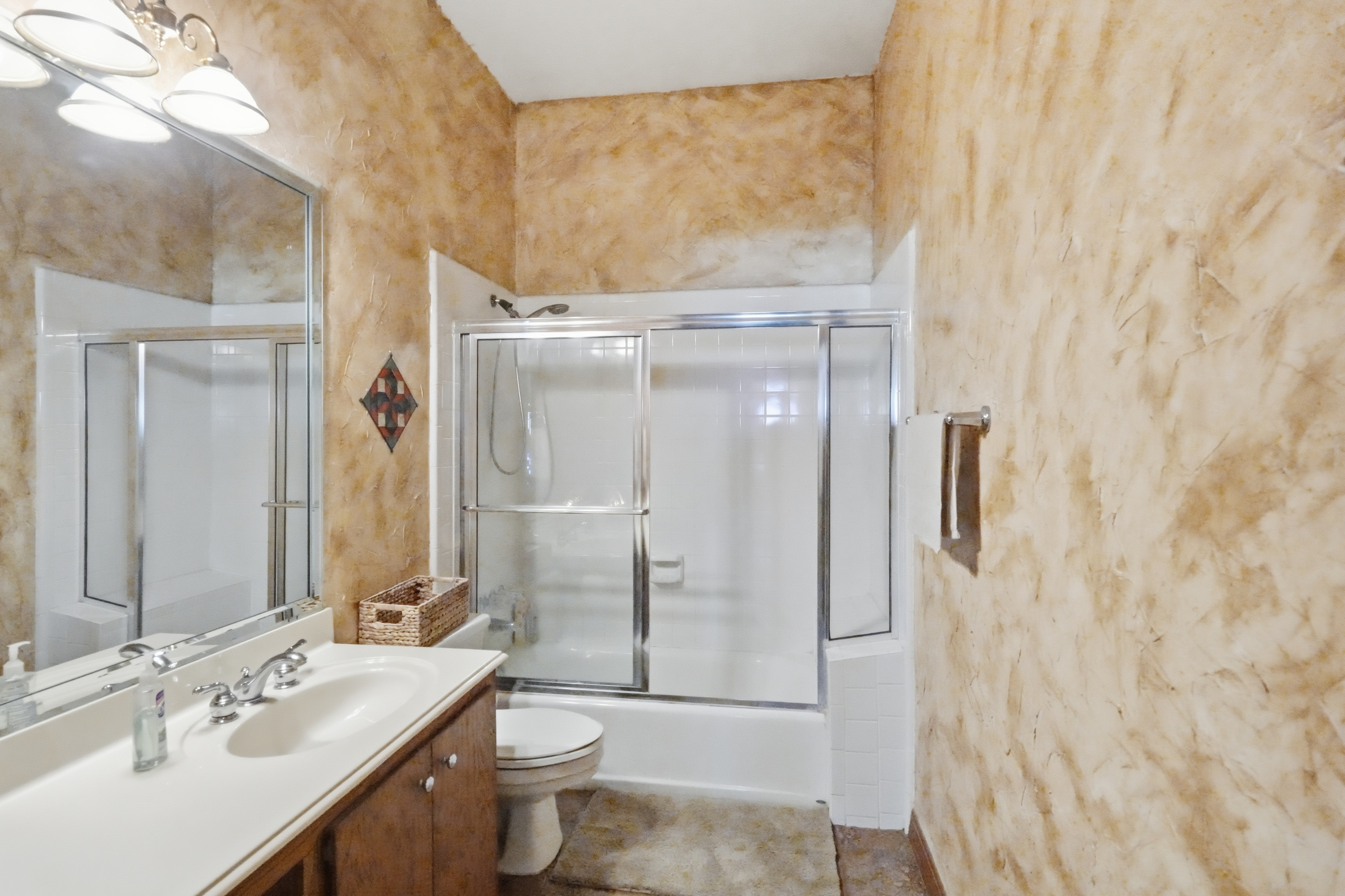Guest bathroom with textured walls, glass-enclosed tub-shower, cultured marble vanity with makeup alcove, and porcelain commode.