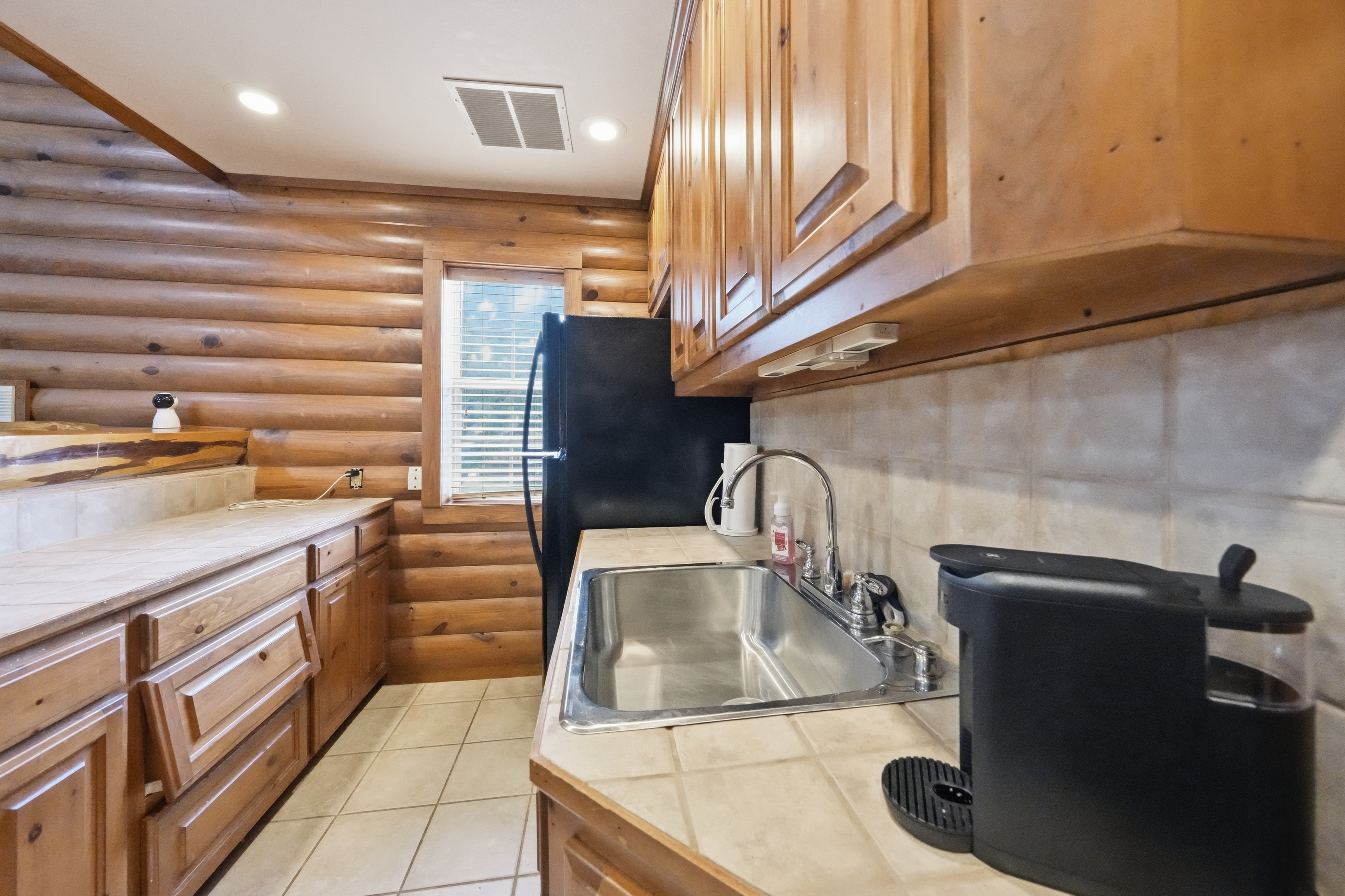 Galley kitchenette with tile counters, stainless steel sink, and stained pine cabinetry.
