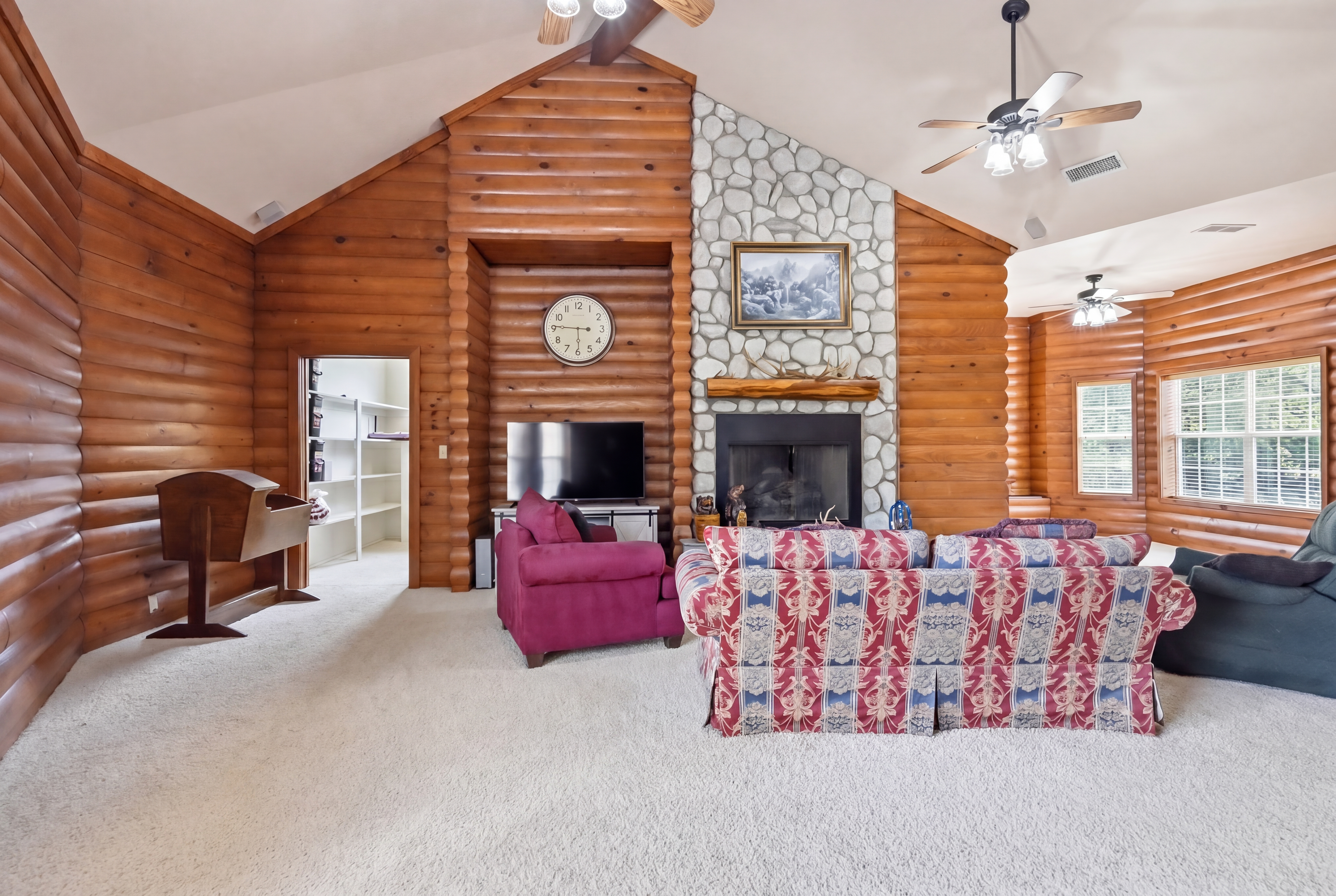 Log-cabin great room with vaulted 15-foot ceiling, hand-laid log walls, river-rock floor-to-ceiling fireplace, and cedar-balustrade loft above.