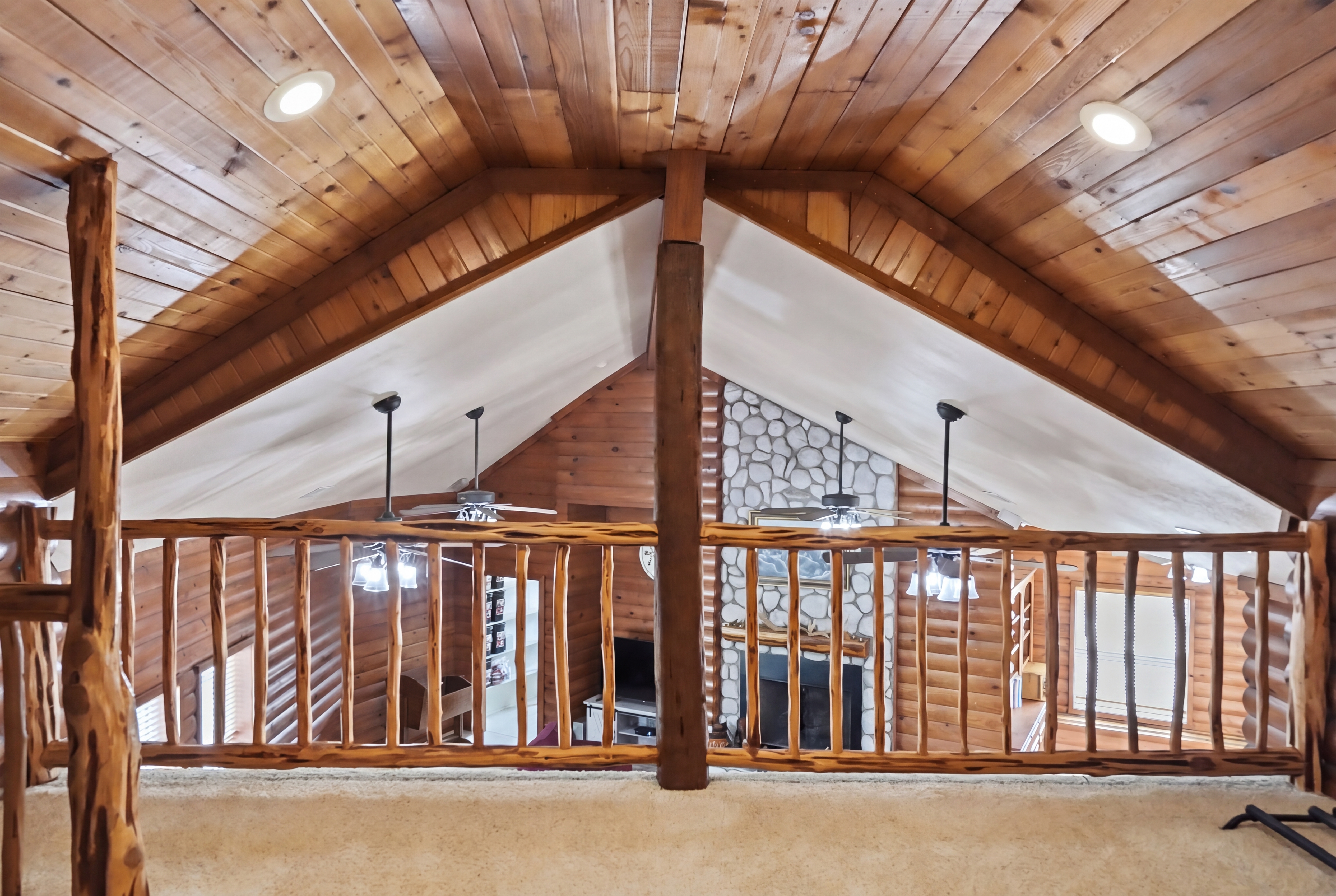 View from the loft looking down to the river-rock fireplace, with cedar-balustrade railing in the foreground.