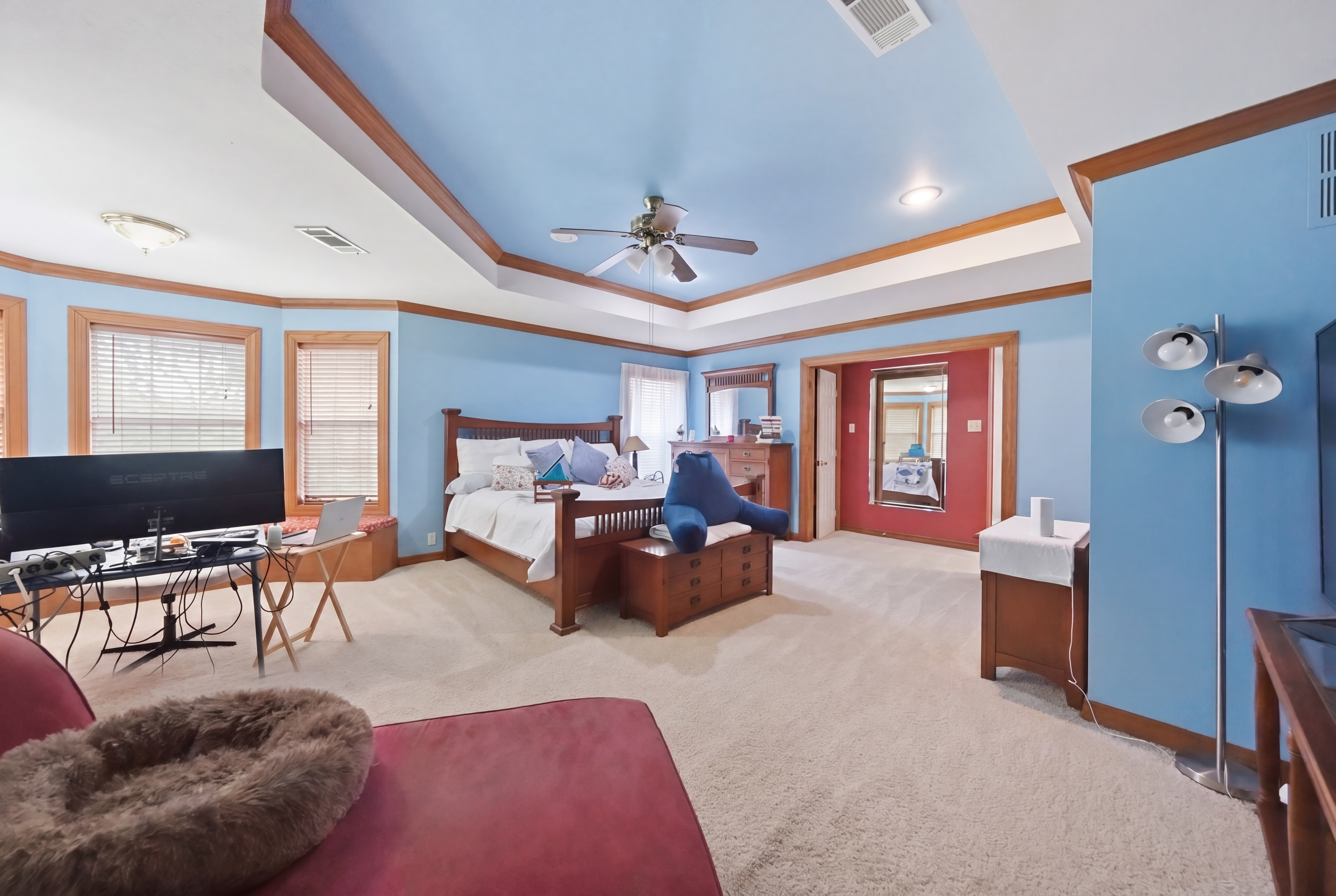 Primary suite with tray ceiling, blue walls, bay-window rotunda, and built-in seating bench overlooking the front yard.