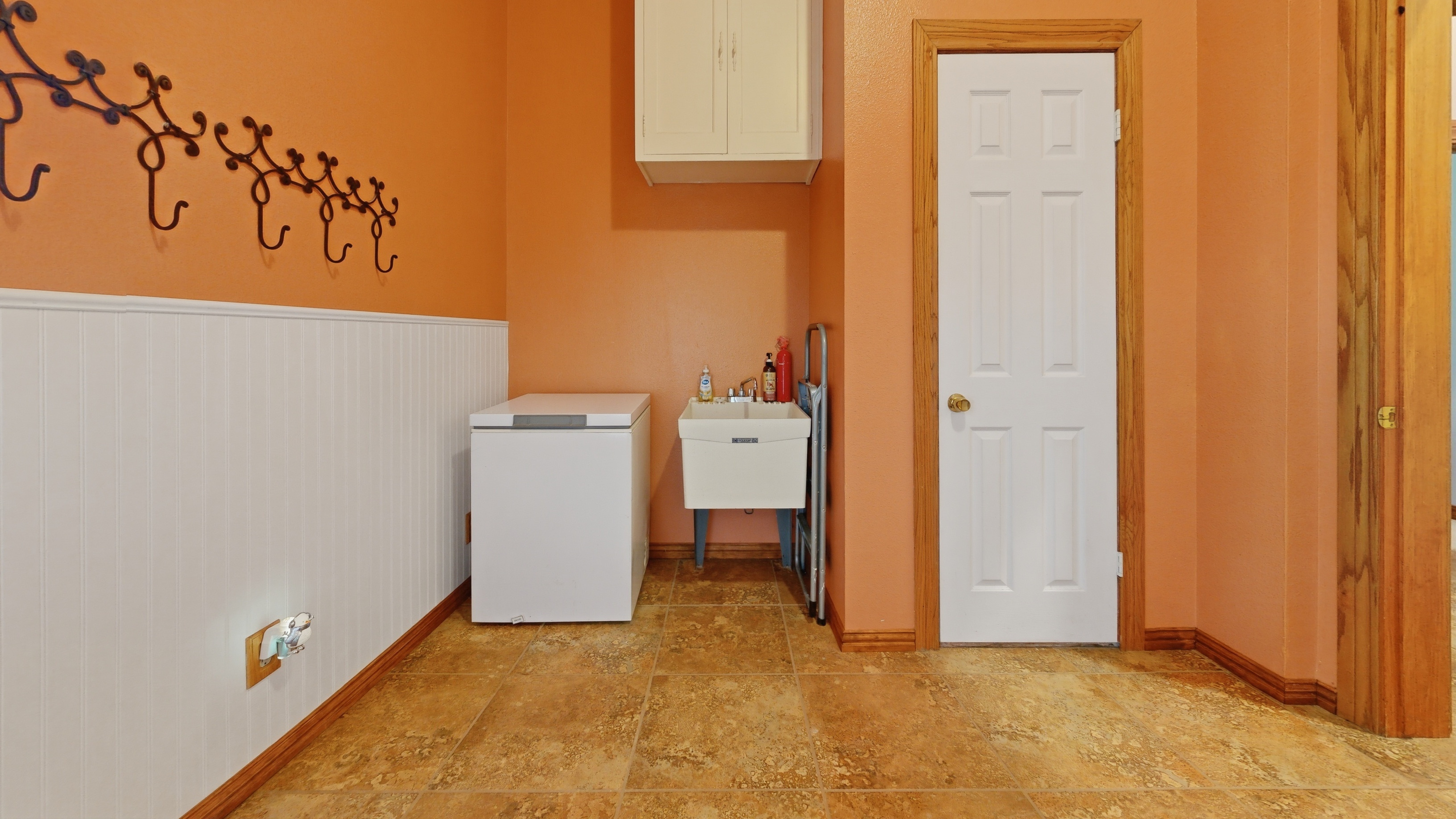 Mudroom with terracotta walls, beadboard wainscoting, large utility sink, and direct garage access.