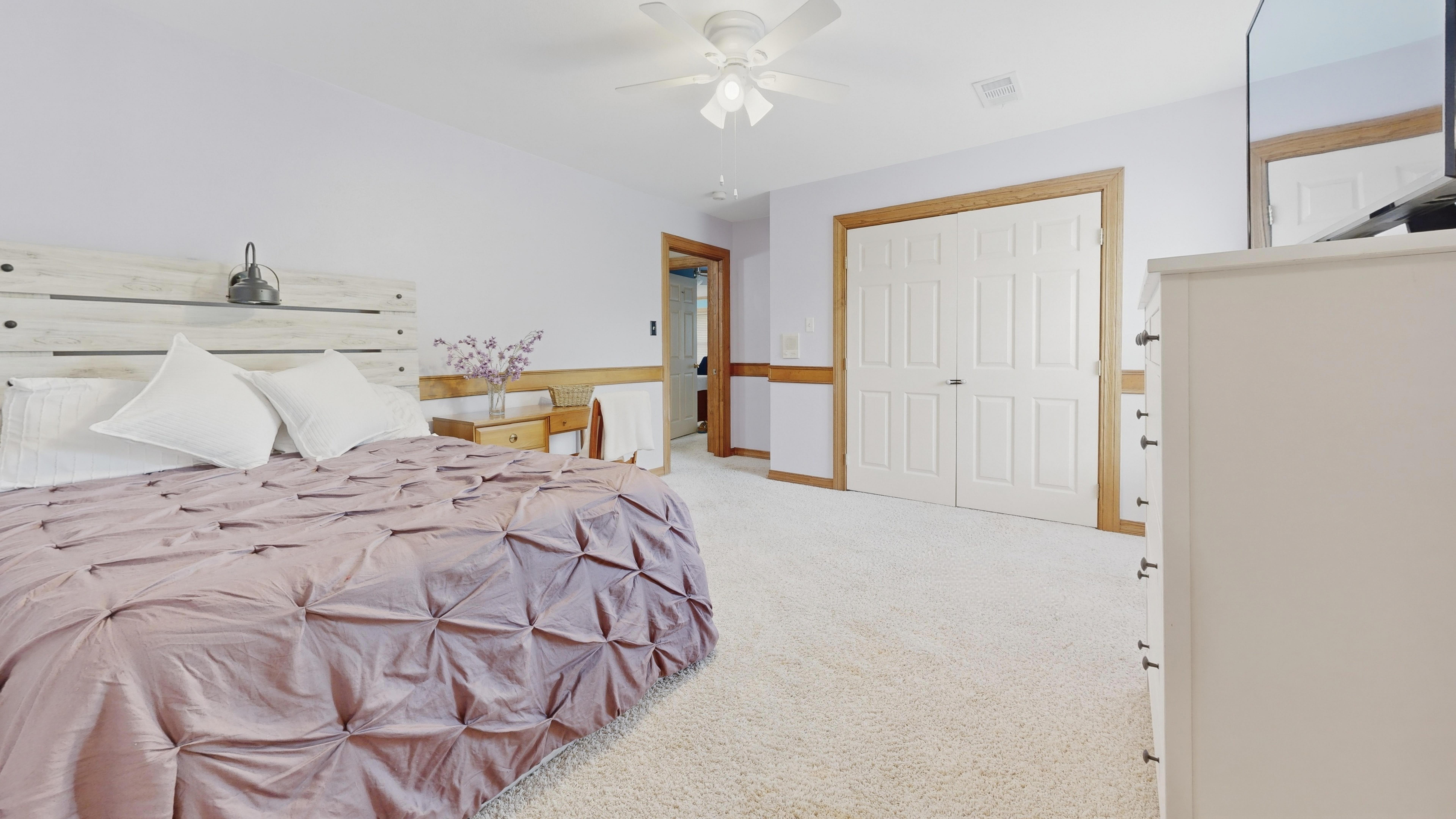 Secondary bedroom with white shiplap headboard, purple bedding, and plush carpet.