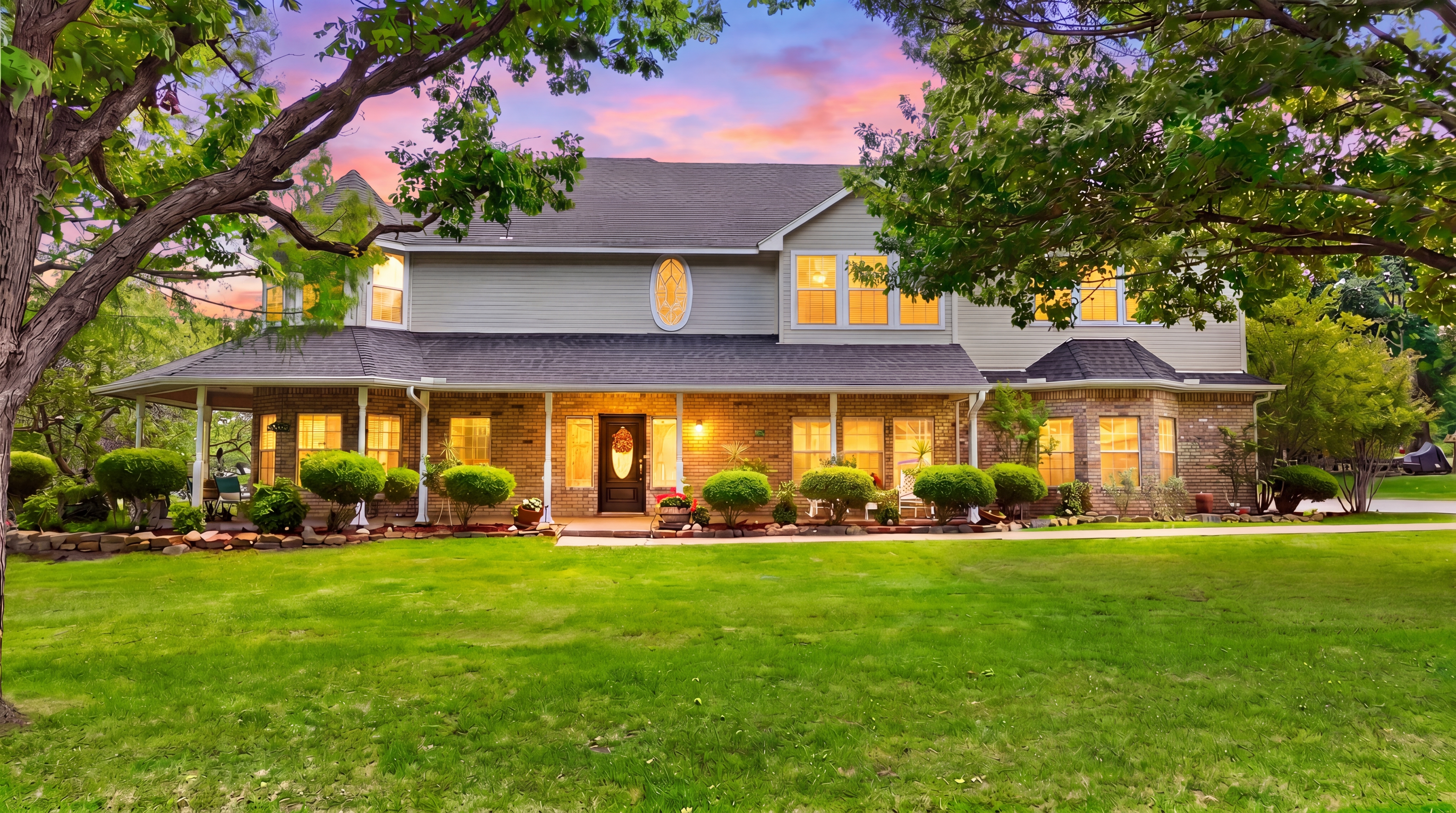Front elevation of 23 Santa Monica Circle at dusk, with mature trees framing the wraparound porch and oval leaded-glass window.